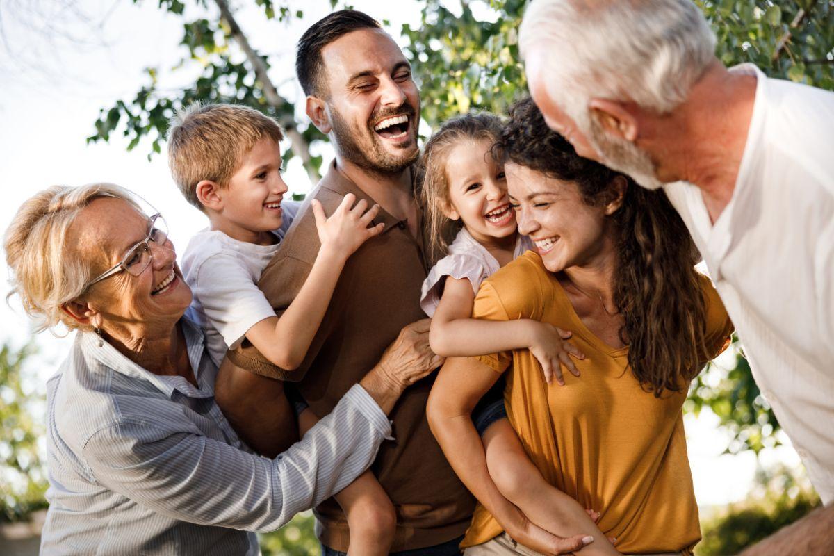 Multi-generational family laughing and embracing outdoors — representing the quality of life that effective pain management can restore